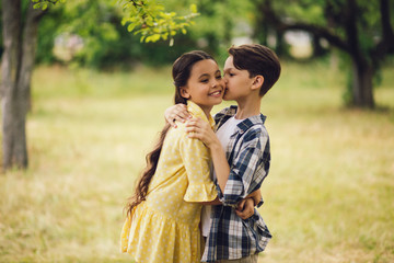Adorable little boy kissing girl. Handsome little man giving his lady kiss on cheek while hugging her. Shot outdoors in nature park.