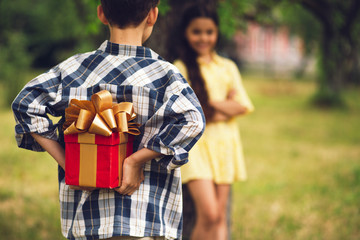 Cute boy preparing to give present to sweet girl. Little boy wearing blue and white button up shirt...