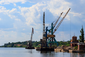 Fototapeta na wymiar Heavy cranes in cargo port on the riverbank