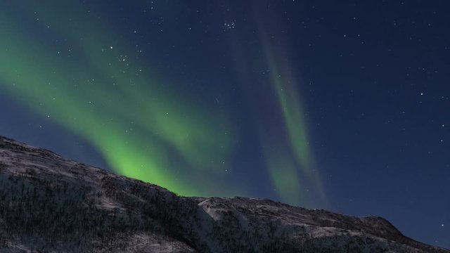 HD Time-lapse of Northern Light Aurora Borealis in the night sky over Senja island in Northern Norway. Snow covered mountains in the background where moonlight is illuminating  landscape.