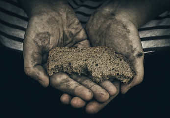 Dirty hands of homeless poor man with piece of bread. The concept of poverty and social inequality.