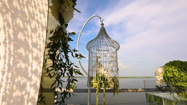 Wedding doves sitting in a cage, White dove sitting in cage on background of river and blue sky, decorative design with flowers and a white dove, wedding decoration