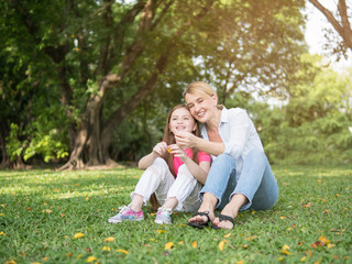 Fototapeta premium Mother and daughter sitting and playing together in the park. Happy family resting together on green grass. Happy family concept.