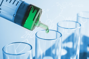 Syringe dropping a chemical solution into a test tube on soft light background.