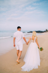 Fototapeta na wymiar newlyweds walking along tropical beach, rear view