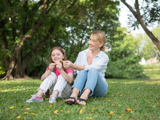 Fototapeta premium Mother and daughter sitting and playing together in the park. Happy family resting together on green grass. Happy family concept.