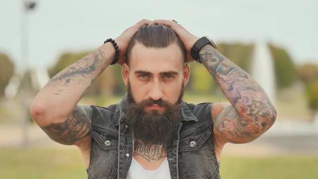 Portrait of a brutal and bearded man with tattoos on his shoulders.