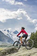 active senior woman, riding her e-mountain bike in the Roseg valley below the glaciers and summits...