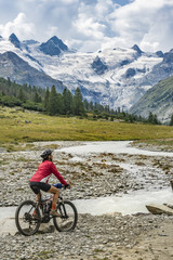 active senior woman, riding her e-mountain bike in the Roseg valley below the glaciers and summits of the Sella Group and Piz Roseg