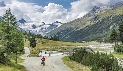 active senior woman, riding her e-mountain bike in the Roseg valley below the glaciers and summits of the Sella Group and Piz Roseg