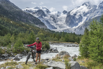 Fototapeta na wymiar Senior woman, riding her e-mountain bike on the trail to the Morteratsch glacier near Pontresina , Engadin, Switzerland,Alps. In the background the famous mountains of Piz palu, Bellavista, Bernina