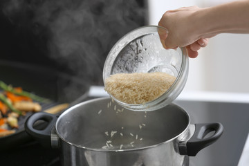 Woman pouring rice into saucepan with boiling water