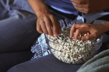 Young couple eating popcorn while watching TV at night, closeup