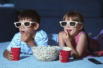 Cute children in 3d glasses watching movie on carpet in evening