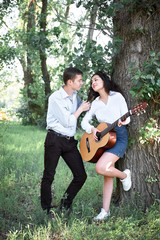 Fototapeta premium young couple walking in the forest and playing guitar, summer nature, bright sunlight, shadows and green leaves, romantic feelings