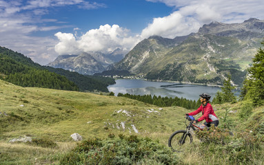 Fototapeta premium Senior woman, riding here e-mountain bike on the famous trails around the lakes in the upper Engadin, between Saint Moritz and Maloja, Engadin, Switzerland with stunning views on the lake of Silvaplan
