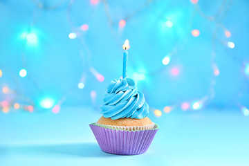 Delicious birthday cupcake with burning candle against blurred lights