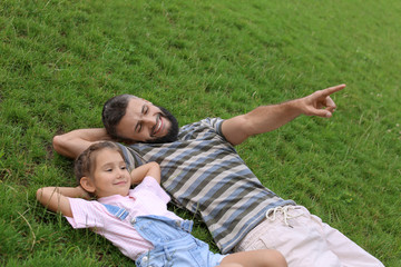 Little girl and her father lying on green grass outdoors
