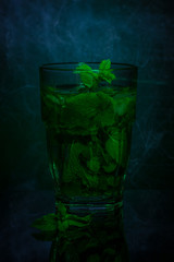 Glass of fresh mint tea on a dark background. Light painting. Copy space.