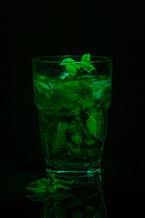 Glass of fresh mint tea on a dark background. Light painting. Copy space.