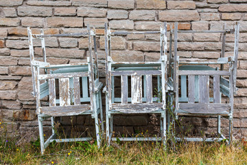 Old leftover garden chairs stacked on a wall in a backyard