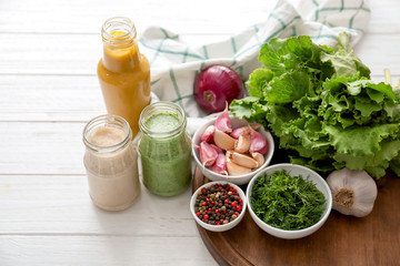 Bottle and jars with different tasty sauces, spices, herbs and vegetables on white wooden table