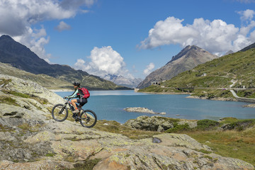 Fototapeta na wymiar senior woman, riding her e-mountainbike on the famous Bernina express trail at Lago Bianco, Bernina Pass near Pontresina an St.Moritz, Engadin, Switzerland