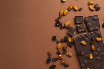 Dark chocolate pieces with roasted almonds and raisins scattered around