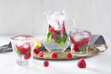 Glasses and jug of fresh raspberry mojito on white table