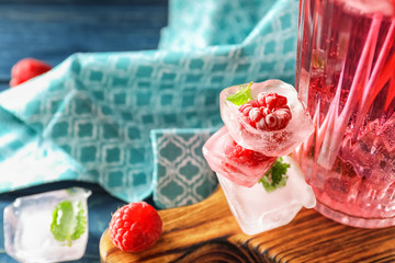 Glass of fresh raspberry mojito and ice cubes on board, closeup