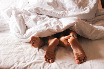 Passionate love. Feet of a young couple that lying on the bed at honeymoon. Couple in love having...