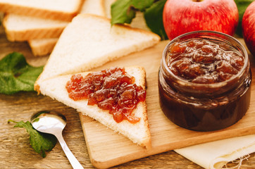 Apple jam on toast and in jar, fresh red apples on a cutting board on a wooden table. Delicious breakfast, rustic style.