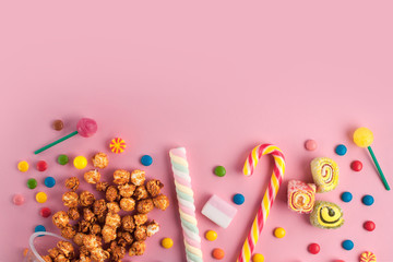 Colored, different sweets, lollipops, marshmallows, caramel popcorn on a pink background. Copy space. Top view