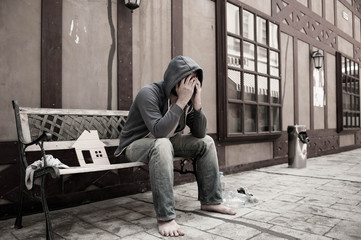 Homeless man sitting on the wooden bench  with his house cardboatd at the city