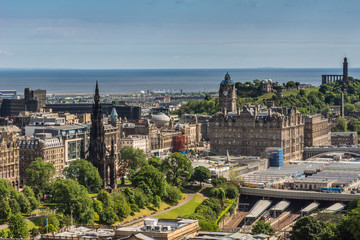 Obraz premium Edinburgh, Scotland, UK - June 14, 2012: Wide view from top of castle towards North Sea inlet with Scott Monument, Balmoral Tower and monuments on Calton Hill under blue sky.