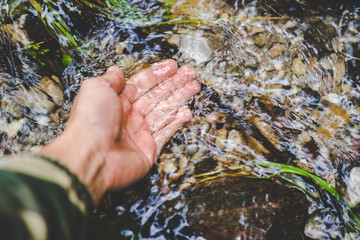 Man hand touching clean, pure, cold water stream