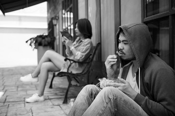 homeless eating food with hungry on street and young women happy with her smartphone sitting on bench