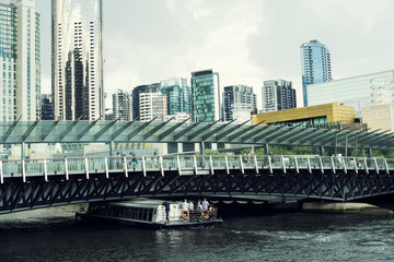 Fototapeta premium Pequeño barco de turistas pasando debajo de un puente moderno frente a un paisaje urbano de edificios altos y rascacielos en una gran ciudad