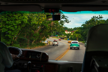 Looking through car window to road, wonderful view of old cars typical of Cuba and a moment of real life.