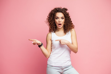 Photo of happy young woman standing isolated over pink wall background. Looking camera showing copyspace pointing.