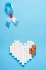 blue ribbon awareness with red blood drop and heart made of sugar cubes on a blue background, world...