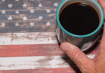 Older male hand with age spots reaching for coffee mug on USA flag table with room for copy text