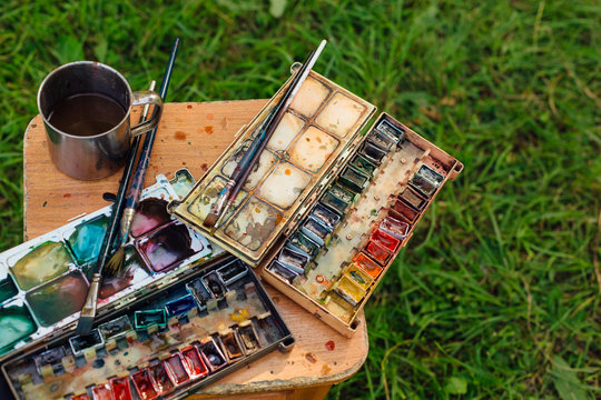 Palette of watercolor paints and brushes on the wooden background.