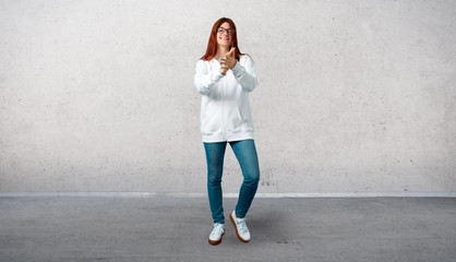 Young redhead girl in an urban white sweatshirt with glasses smiling and applauding and standing on...