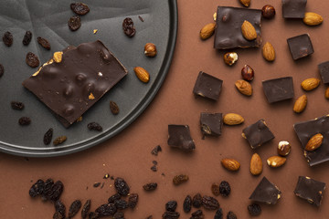 Dark chocolate pieces with roasted almonds and raisins scattered around