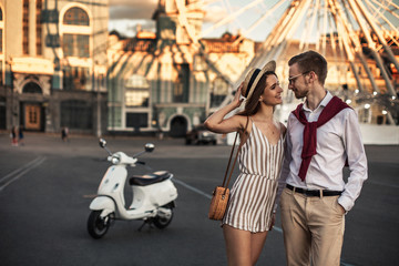 Husband and wife on a walk with a white moped in the city near the Ferris wheel