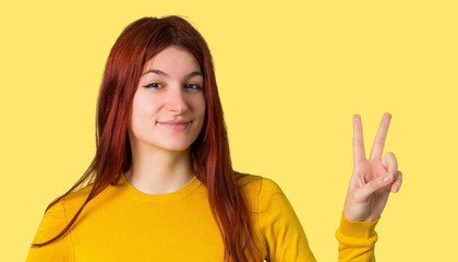 Young redhead girl with yellow sweater happy and counting two with fingers on isolated yellow background