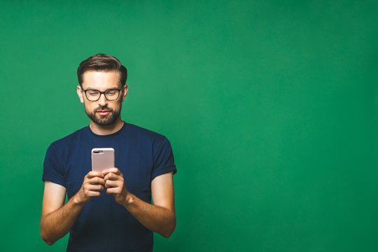 Always In Touch. Smiling Young Man Holding Smart Phone And Looking At It. Portrait Of A Happy Man Using Mobile Phone Isolated Over Green Background.