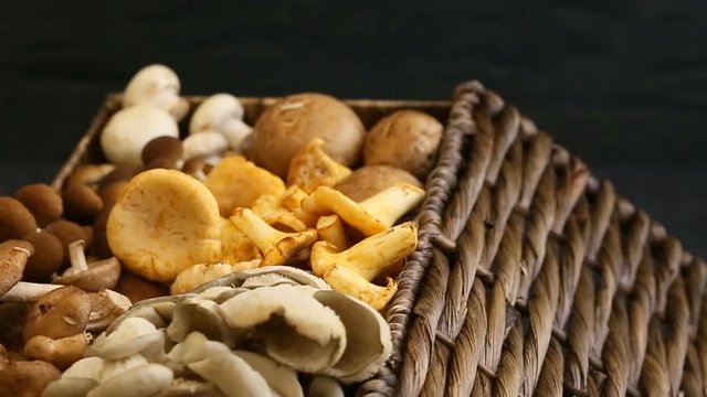 Variety of uncooked wild forest mushrooms in a wicker basket on a black background, Rotation 360. Mushrooms chanterelles, honey agarics, oyster mushrooms, champignons, portobello, shiitake