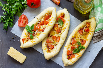 Delicious homemade Greek oval pizza with salami, tomato, onion and cheese on a dark stone background. Copy space, top view flat lay background.